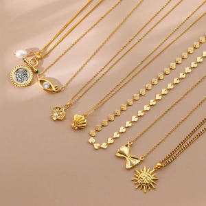 Close-up of gold plated necklaces with sun, bow, and evil eye pendants on beige background