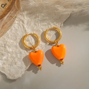 Boucles d'oreilles créoles dorées avec cœurs orange et perles sur papier texturé