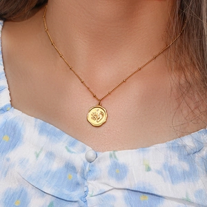 Détail du pendentif pièce empreinte bébé dorée sur collier à billes porté par un mannequin
