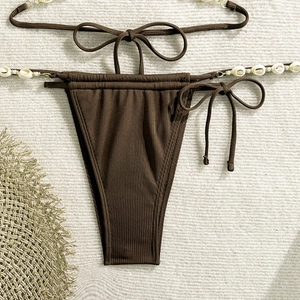 Detail of dark brown ribbed bikini bottoms featuring shell and bead ties on neutral background