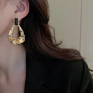 Detail of gold wrinkled geometric earrings with black gemstone worn by a model