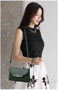 Detail of dark green pebble leather crossbody bag with silver curved metal buckle on model