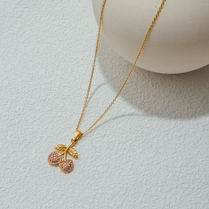 Detail view of gold cherry pendant necklace featuring pink crystal stones on white surface