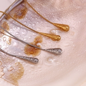 Detail of gold and silver teardrop pendants with hammered texture on a pearly surface