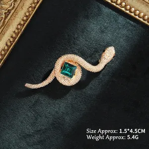 Detailed view of snake brooch with green crystal and gold metal on velvet background