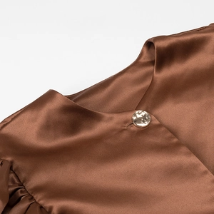Detail shot of the glossy brown satin shirt neckline featuring a golden metal button accent