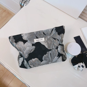 Elegant black and silver floral jacquard cosmetic bag with a chic woven brand label