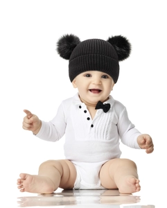 Close-up of black knitted baby hat with dual pom-poms and white romper outfit