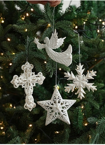 White glitter angel and star ornaments hanging on a Christmas tree with warm lights