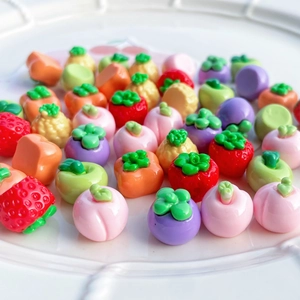 Mini ciondoli in resina a forma di frutta come fragola e pesca su un piatto bianco