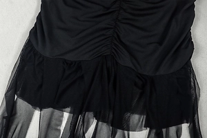 Detail view of black bodycon dress featuring pleated ruched design and mesh patchwork hem