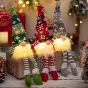 Three glowing Christmas gnomes with knitted snowflake hats and striped legs on wood