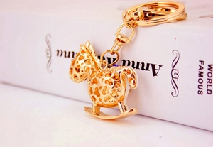 Close-up of golden hollow rocking horse keychain with lobster clasp on a white book