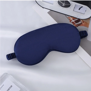 Close-up of a dark blue silk sleep mask with elastic strap on a white fabric background