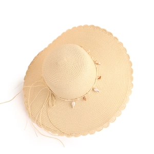 Close-up of beige straw sun hat featuring wavy edges and decorative white seashells