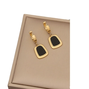 Golden geometric earrings with black trapezoid enamel inlay on a beige leather background