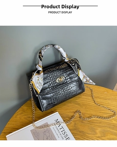 Detail of black crocodile texture bag with decorative silk scarf and gold chain