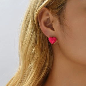 Close-up of hot pink heart enamel earrings worn by a model to show texture and size
