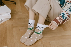 Detail of plush coral fleece winter socks with elk pattern on wooden floor