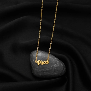 Pisces zodiac necklace with gold letter pendant on thin chain over dark silk background