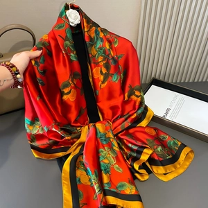 Elegant red silk scarf with orange and leaf prints hanging gracefully by a handbag