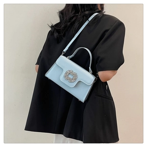 Détail du sac bandoulière bleu clair avec boucle strass sur un blazer noir chic