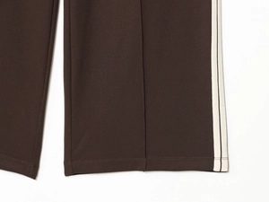Detail of dark brown sweatpants featuring white side stripes and fine stitching at the hem
