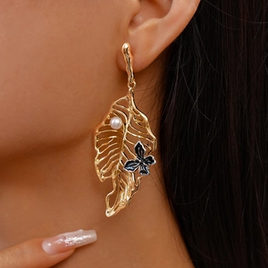 Detailed close-up of a gold hollow leaf earring with pearl and butterfly on model