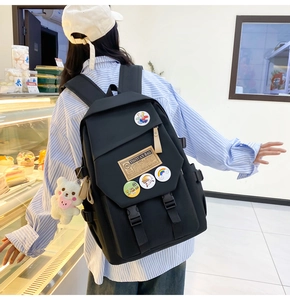 Detailed back view of black nylon student backpack with cute badges and plush bear charm