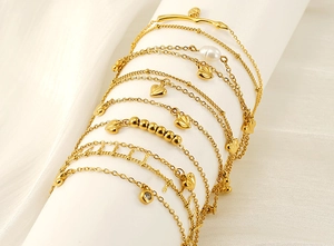 Macro detail of layered 18K gold plated anklets with pearls and heart charms on a stand
