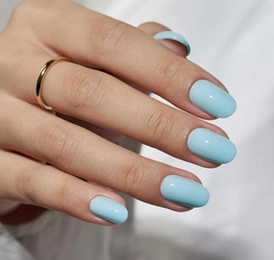 Primer plano de uñas almendradas azul claro brillante con un anillo de oro minimalista