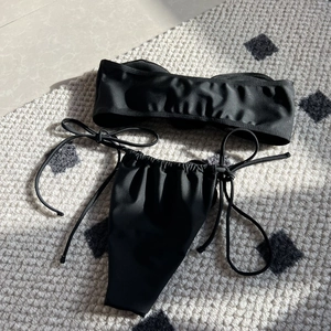 Detailed flat lay of black bandeau bikini set with side-tie bottoms on textured rug