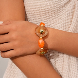 Detail of beaded necklace with orange resin charms and golden metallic spheres