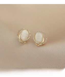 Detail of oval cat eye opal earrings with sparkling zircon halo on champagne silk fabric