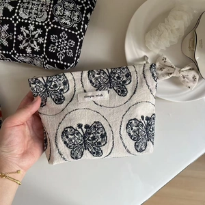 Detailed embroidery of a blue butterfly on a beige cotton-linen cosmetic pouch with zipper