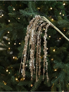 Detail of glittery gold Christmas spray branches hanging on a lighted green festive tree