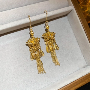Detail von goldenen Lotus-Ohrringen mit feinen Quastenketten auf grauem Samt-Display