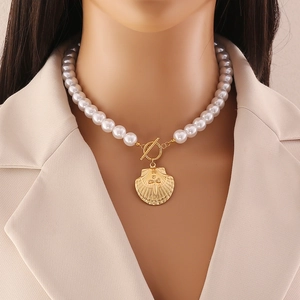 Seashell and pearl stainless steel necklace with gold pendant on model wearing beige suit