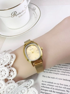 Close-up of golden oval quartz watch with mesh band worn by a woman reading a book