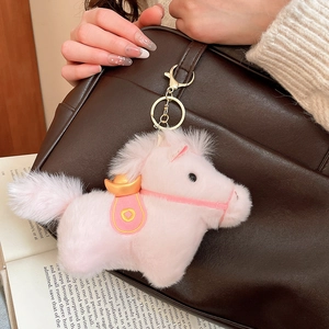 Dettaglio di un ciondolo a forma di pony in peluche rosa appeso a una borsa di pelle