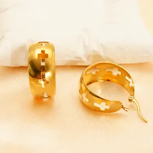 Golden wide-band hoop earrings featuring minimalist cross patterns on warm satin background