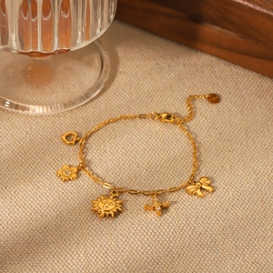 Gold-plated stainless steel bracelet featuring heart, sun, and flower charms on beige fabric