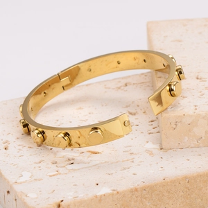Detail showing polished gold-plated bangle with rivet stud on textured stone base