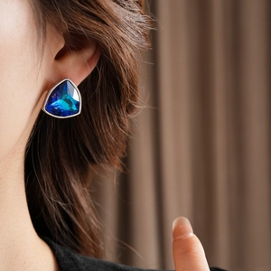 Vue macro de boucles d'oreilles triangulaires en argent avec cristaux bleus sur l'oreille