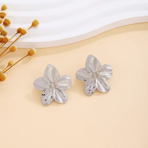Detailed view of silver flower earrings with textured petals on a cream display