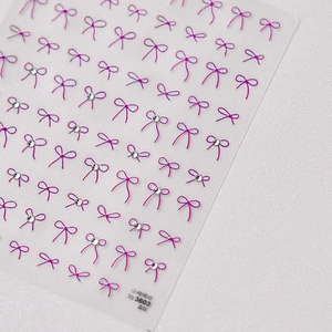 Macro shot of 3D pink bow nail art stickers with sparkly crystal accents on white surface