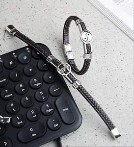 Braided leather bracelets featuring silver treble clef and Tai Chi charms on a keyboard