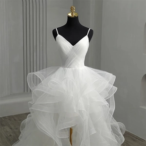 Detail of deep V-neck white wedding dress with pleats and layered ruffled tulle skirt