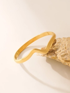 Close-up of golden wavy cuff bracelet displayed on raw natural stone background