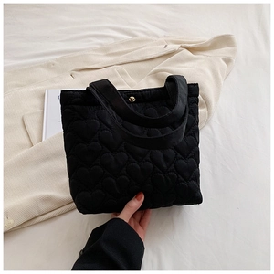 Detail of black heart quilted tote bag with gold metal buckle on white fabric